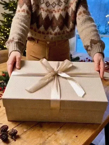Hands lifting the lid off the kraft gift box and raising the lit ornament out of it